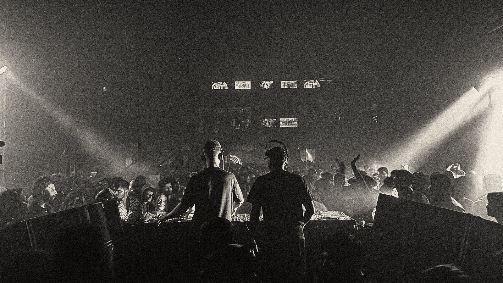 Dos DJs tras la cabina frente al público, entre humo y haces de luz